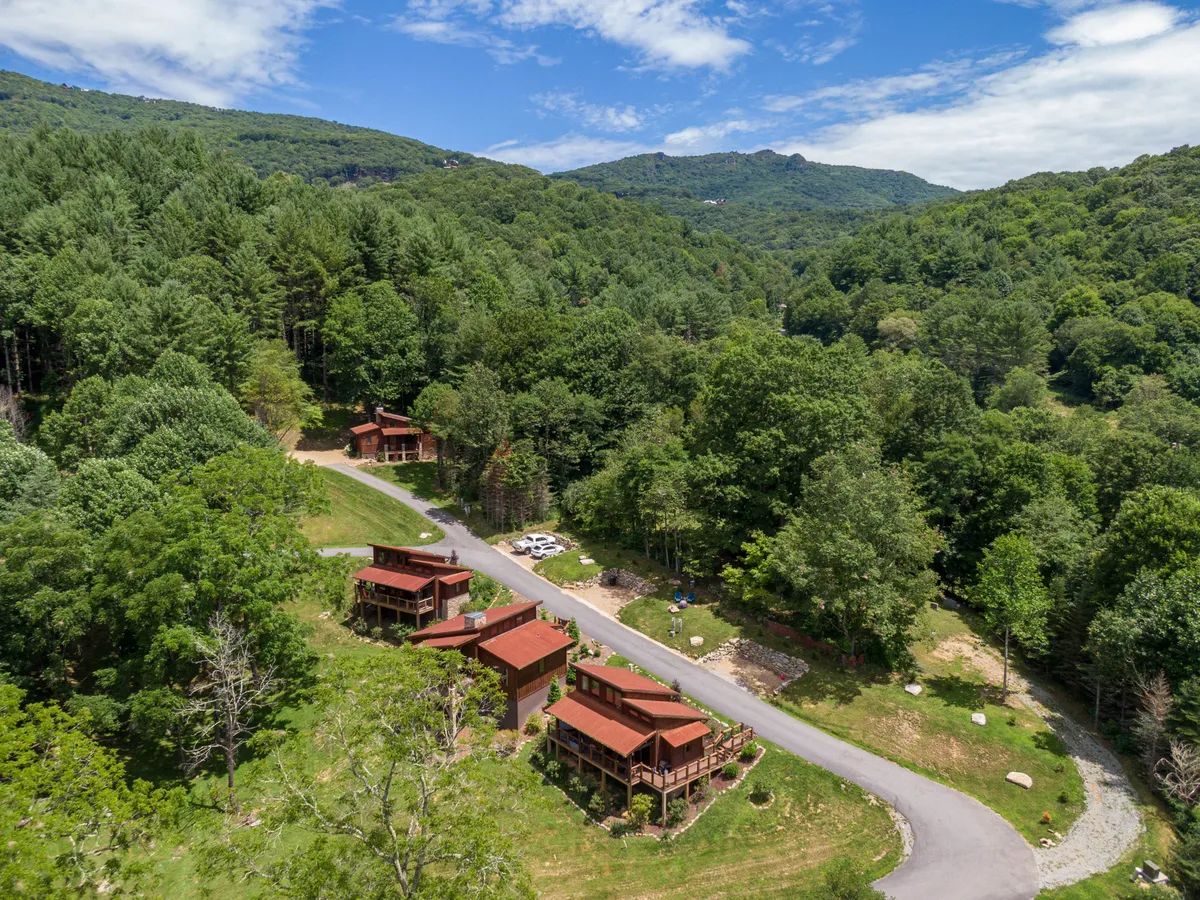 This image features several cabins nestled along a road, surrounded by lush trees and mountains in the backdrop. The open space and natural setting hint at both the peaceful environment and the scope of amenities and activities available within the community.
