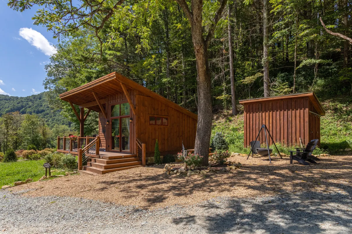 A tranquil exterior shot featuring the wooden cabin, a cozy outdoor seating area, and landscaped grounds. The adjacent storage shed and ample seating suggest a functional, relaxed space for barbecues or resting after a day outside with your dog.