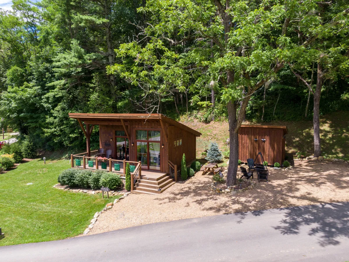 A wooden cabin with a welcoming outdoor seating area, set against a background of rich greenery. The image evokes relaxation, socializing, and enjoying the natural surroundings—key aspects of both private living and community amenities.